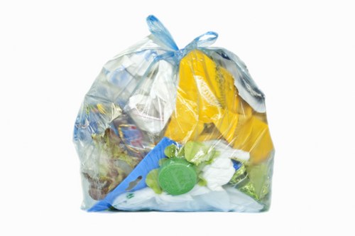 A transparent plastic bag filled with various household rubbish materials sits on a flat surface. Inside the bag, there are crumpled paper, plastic containers, and packaging, with some items visibly made of plastic with smooth, glossy finishes in colours such as yellow, blue, and green. The bag appears to be tied at the top with a small loop of plastic, and the contents are slightly bulging, indicating it is full. The background is plain and neutral, with no additional objects or environmental details visible. This image exemplifies typical waste items collected during rubbish removal services, as offered by Commercial Waste Stevenage, situated within the Stevenage area, close to SG postcode. It visually represents general household waste ready for collection, highlighting plastic packaging and other refuse commonly managed by commercial waste removal providers in the region.